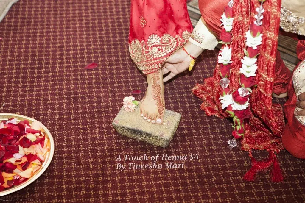Bride Nalini's wedding mehndi-covered foot stepping on ritual stone during Hindu ceremony