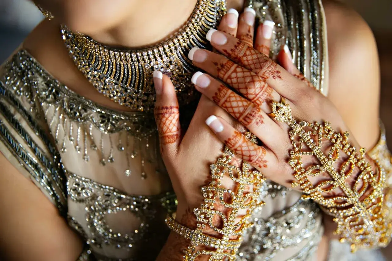 Bride in gold embroidered dress with mehndi on hands and engagement ring, hands crossed on chest