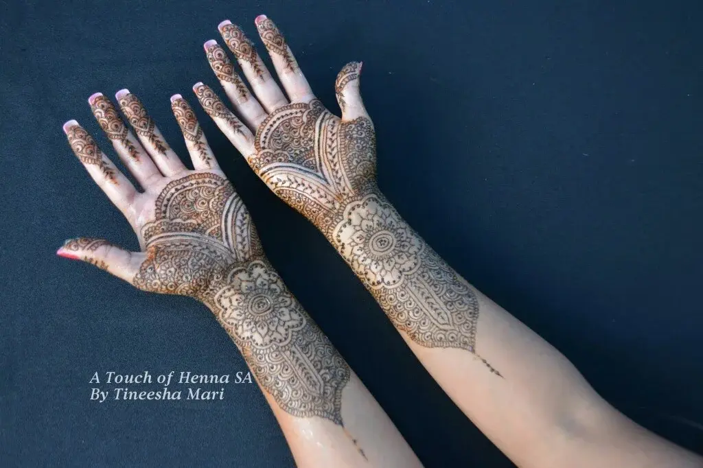 Full-arm bridal mehndi with dense floral and mandala patterns on both hands and forearms, professional photography
