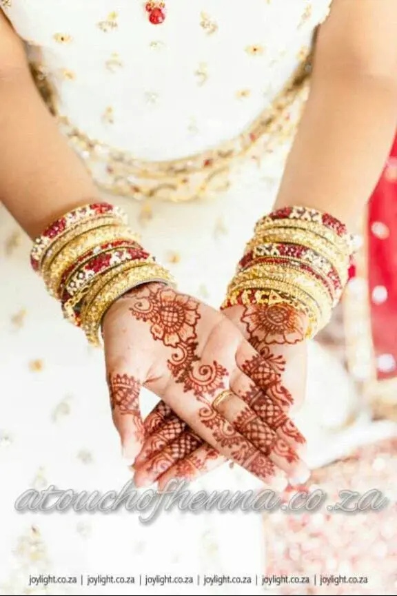 Bride displaying full-palm bridal mehndi with gold bangles against white lehenga, professional photography