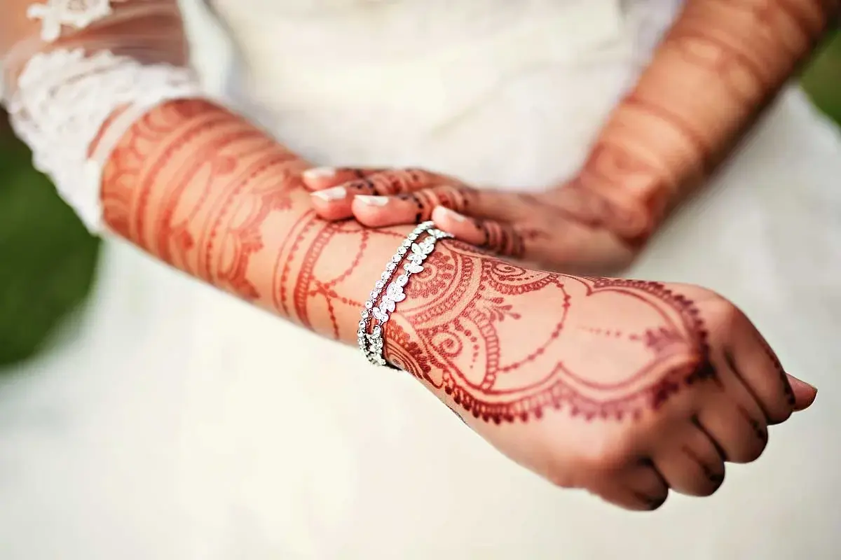 Close-up of bridal mehndi arms crossed, large flowing paisley design on forearms with diamond bracelet